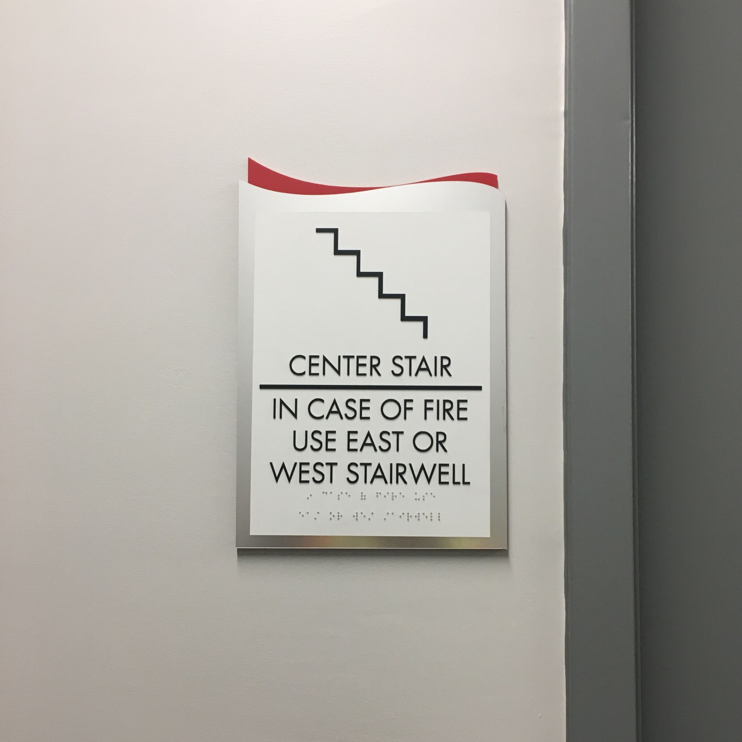 Sign reading "IN CASE OF FIRE USE EAST OR WEST STAIRWELL" in tactile characters and Braille.