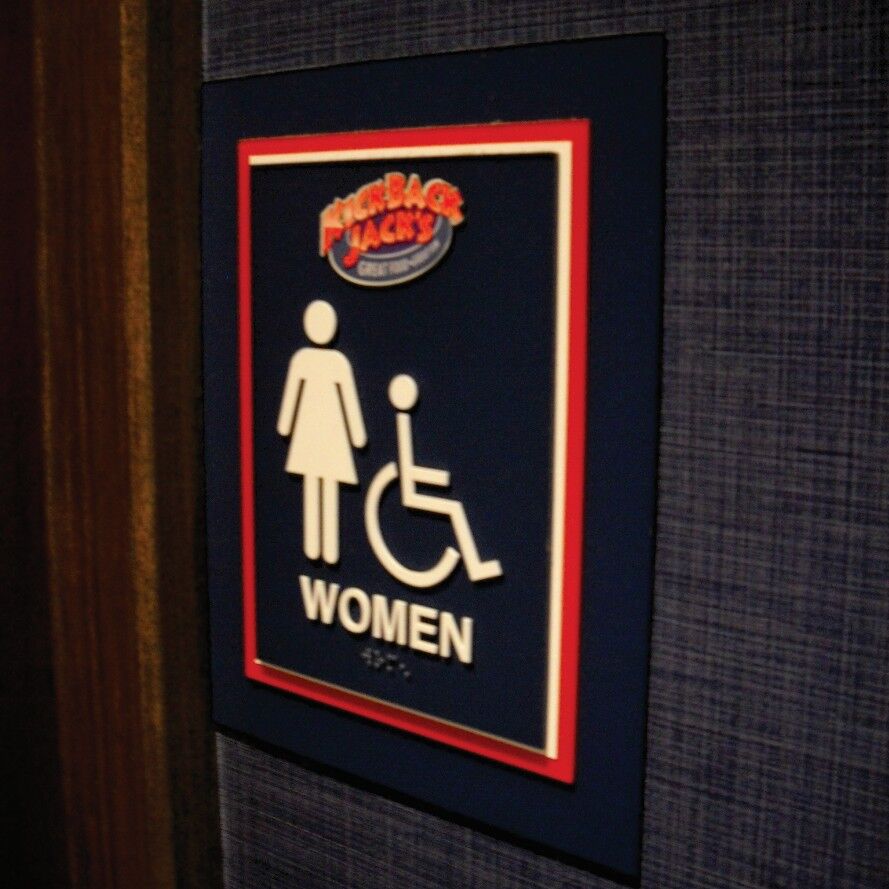 Bathroom sign for women with Braille underneath the written text.